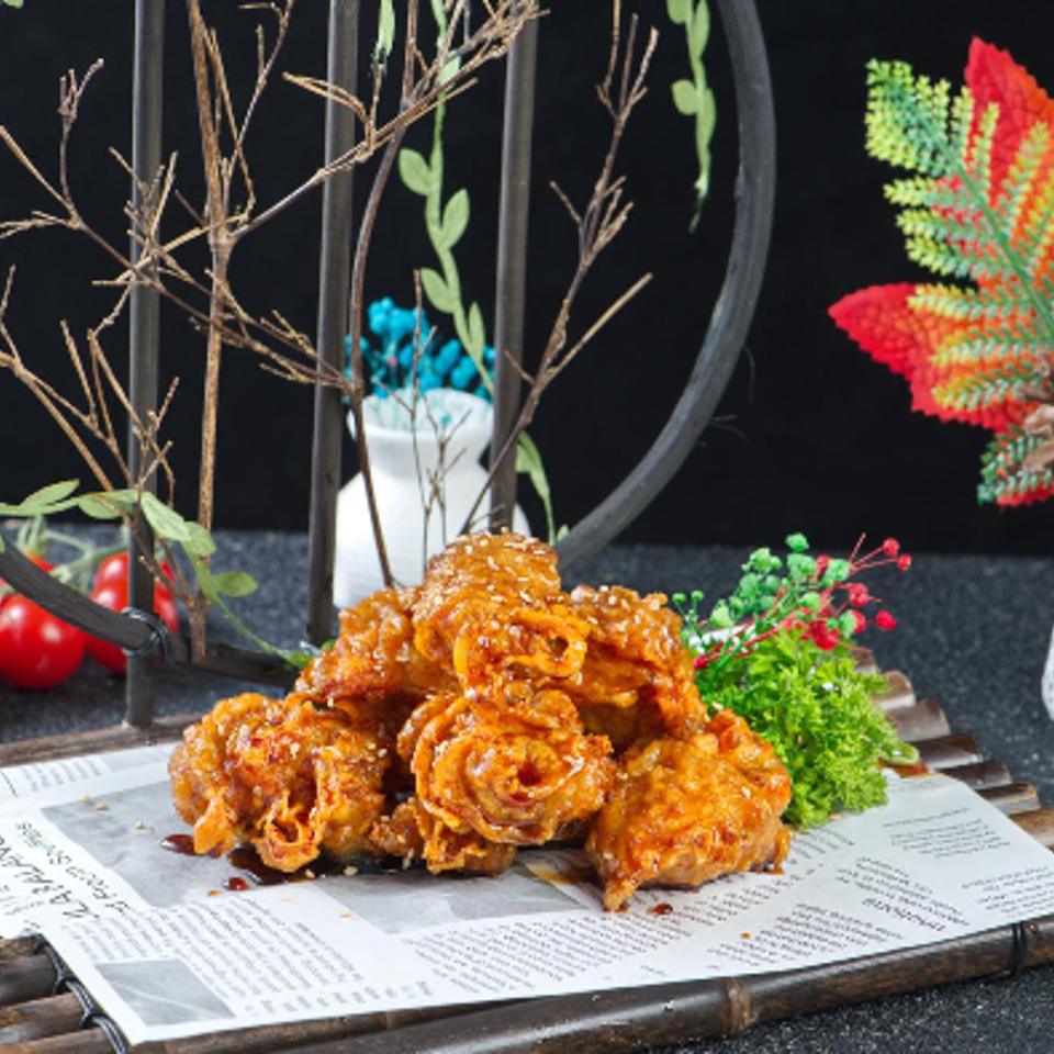 Pile of crispy fried chicken wings glazed in sauce, garnished with parsley and berries, displayed on a newspaper-covered table.