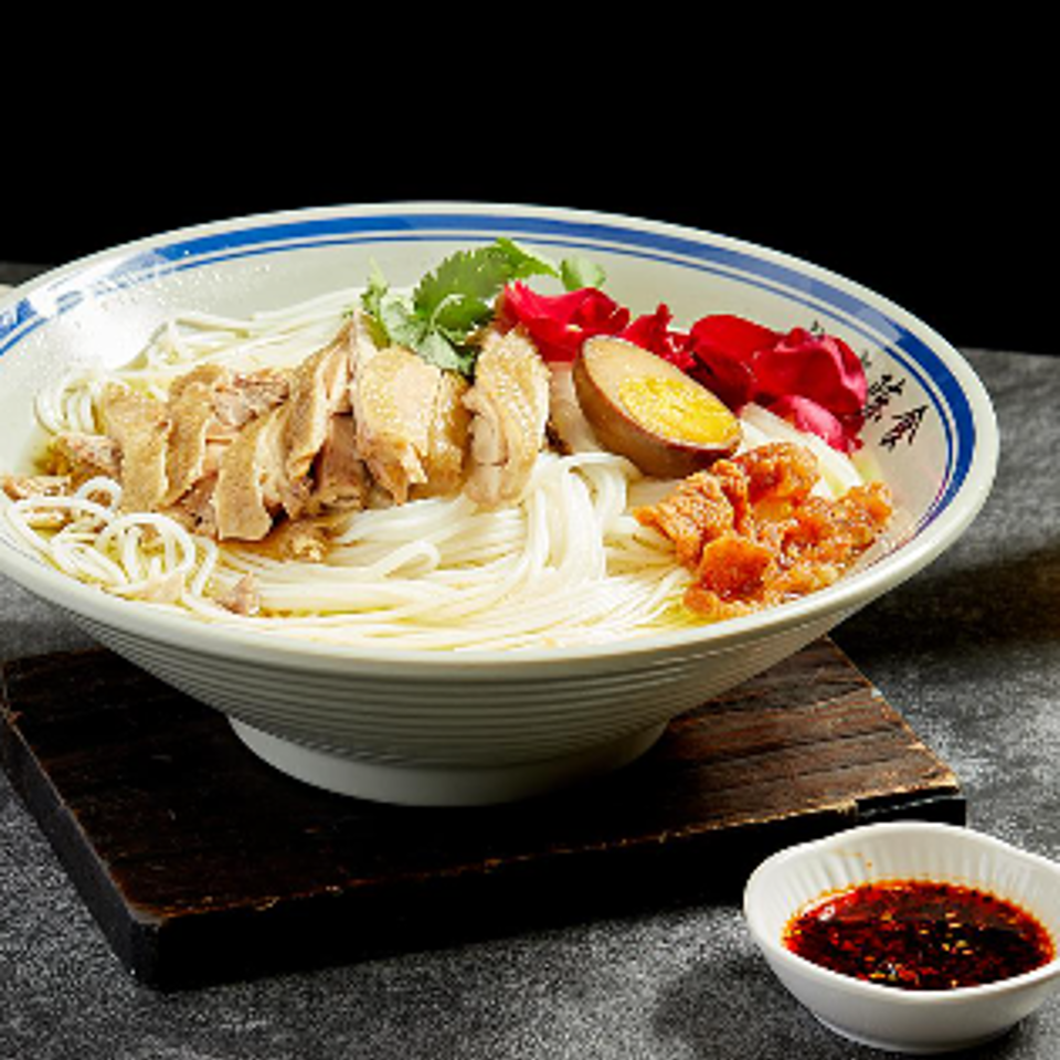 Bowl of chicken, noodles, shrimp, vegetables, and lemon with dipping sauce on a dark wooden tray.