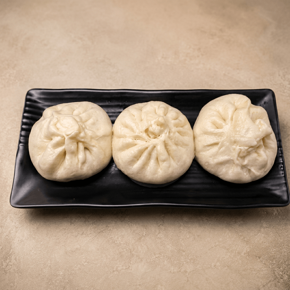 Three steamed dumplings with pleated tops arranged on a black rectangular plate.