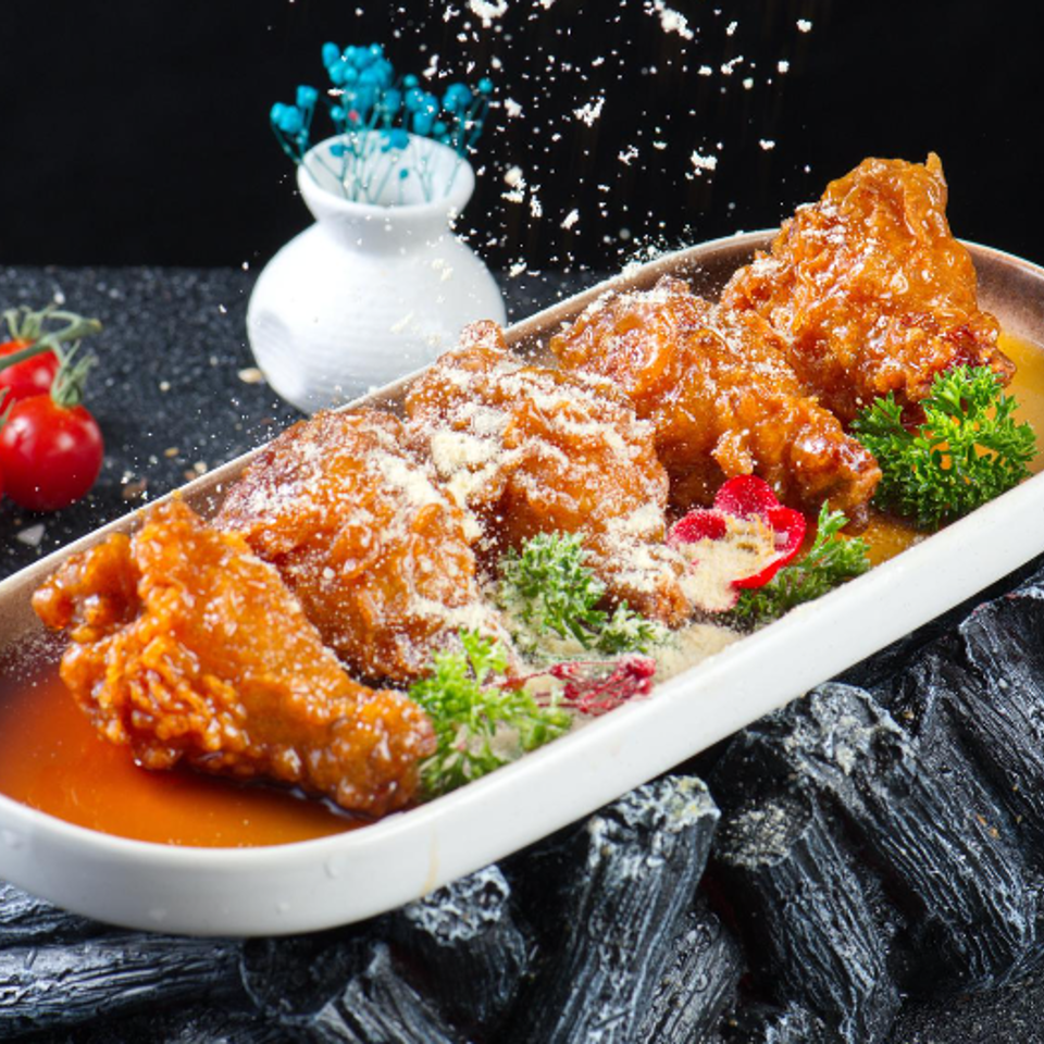 Crispy fried chicken wings coated in orange sauce, garnished with herbs and powdered seasoning in a white dish.