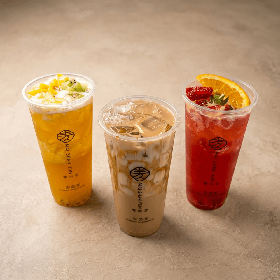 Three Mai Shan Yun drinks in branded cups: a golden fruit tea, creamy iced beverage, and red strawberry-orange drink.
