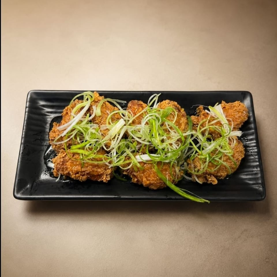 Crispy glazed fried chicken pieces topped with sliced green onions on a black rectangular plate.